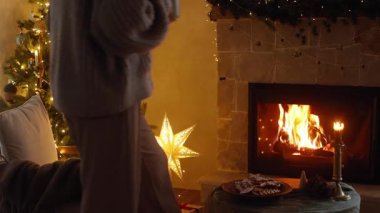 Sıcak Noel arifesinde şöminede dinlenme zamanı. Sıcak kazaklı bir kadın Noel şenlik odasında şöminede rahatlıyor ve sıcak çay içiyor. Kış kızlık zarı görüntüleri