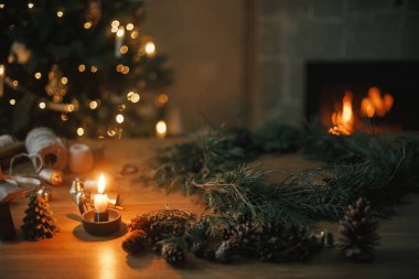 Noel kırsal çelengi yapıyorum. Sedir dalları, çam kozalakları, mum, sicim, akşam odasındaki ağaç ve şömineye karşı ahşap masada çanlar. Kış tatili hazırlıkları, atmosferik zaman