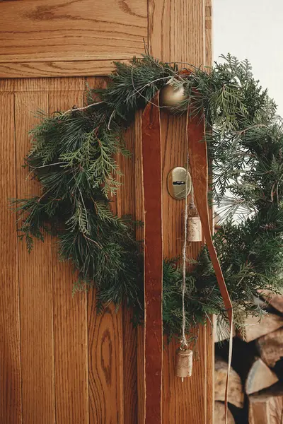 风格别致的圣诞乡村花环 在木门上的黄铜把手上挂着老式铃铛和彩带 冬季度假装饰的现代农舍外入口 圣诞快乐 — 图库照片
