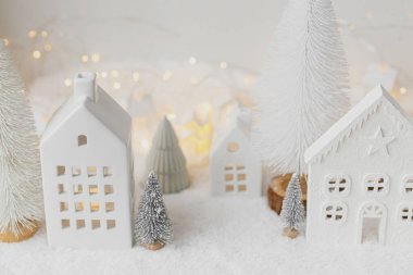Sıcak Noel minyatür köyü. Küçük seramik evler ve kar örtüsü üzerinde ağaçlar beyaz arka planda altın ışıklar. Atmosferik kış köyü modern natürmort. Mutlu Noeller.!