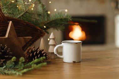 Şık bir fincan sıcak çay, köknar dalları, tahta ağaçlar ve yıldız, şöminenin karşısında duran kozalaklar. Modern Noel kırsal çevre dostu dekor ve kupa, İskandinav kış ikilisi