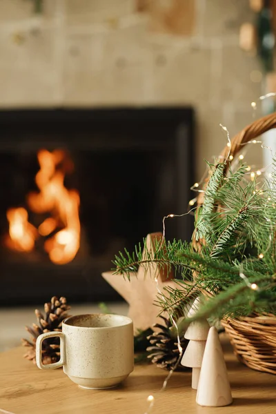 暖かいお茶のスタイリッシュなカップ 火の枝 木の木 火の暖炉に対してテーブルの上の松のコーン 冬の休日のための現代クリスマス素朴なエコフレンドリーな装飾 — ストック写真