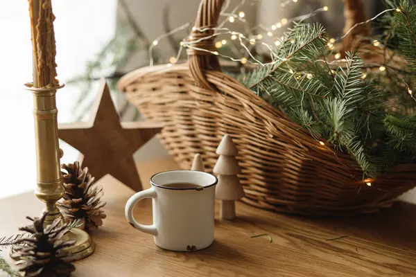 スカンジナビアの衛生 暖かいお茶のスタイリッシュなカップ バスケットの枝 木の木 テーブルの上の松のコーンおよびライト モダンなクリスマス素朴なエコフレンドリーな装飾とカップモックアップ — ストック写真