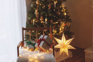Modern dekore edilmiş altın ışıklı ve parlak yıldızlı Noel ağacının arka planında şık Noel hediyeleri. İskandinav odasında atmosferik noel arifesi. Mutlu Noeller.!