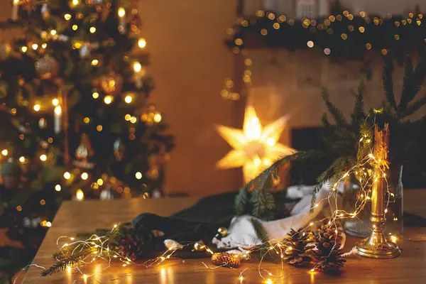 スタイリッシュなキャンドル ゴールデンライト 松のコーン お祝いのイルミネーションとスタイリッシュな装飾クリスマスツリーと暖炉に対する木のテーブルの装飾 お祝いの家で大気の冬の休日 — ストック写真