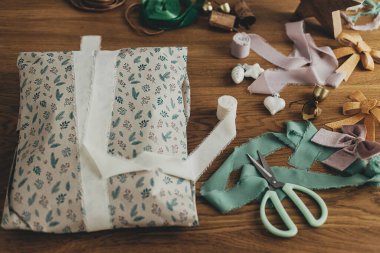 Şenlikli hediye, şenlikli ambalaj kağıdı, kurdele, makas, fiyonk, eski süsler ve ahşap masada pirinç çanlar. Noel hediyelerini paketliyorum. Kış tatili hazırlığı