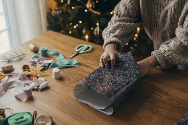 Noel hediyelerini paketliyorum. Ellerin rahat süveter içinde şık bir hediye paketinin içinde kurdelelerle, eski süslemelerle, ahşap masanın üzerinde fiyonklarla. Atmosferik kış tatili