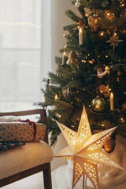 Mutlu Noeller! Şenlikli yılbaşı hediyeleri, fiyonklu şenlik kağıtlarına sarılmış Noel ağacı ışıkları ve altın yıldızlı arka planda modern koltukta eski oyuncaklar. Atmosferik kış tatili