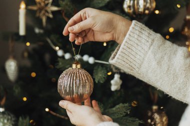 Noel ağacını şık takılarla süslemek. Eller rahat süveter içinde ağaç dalına asılmış eski püskü süsler. Atmosferik kış tatili geleneği, aile zamanı