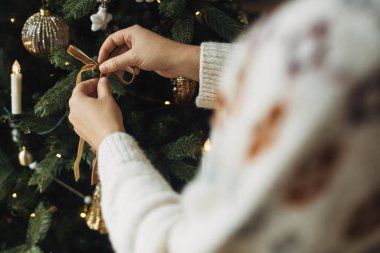 Eller rahat süveter içinde ağaç dalına modern kadife süslemeler asıyor. Noel ağacını şık bir kurdeleyle süslemek. Atmosferik kış tatili geleneği, aile zamanı