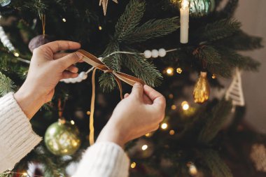 Noel ağacını şık bir kurdeleyle süslemek. Konforlu kazaklı bir kadın ağaç dalına modern kadife süslemeler asıyor. Atmosferik kış tatili geleneği, aile zamanı