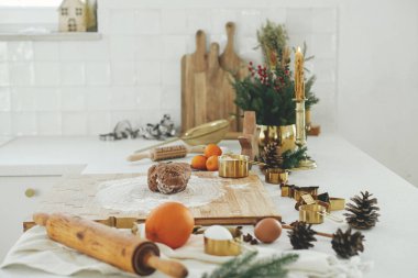 Modern beyaz mutfakta zencefilli kurabiye yapıyorum. Tahtada zencefilli ekmek hamuru, un, merdane, altın metal kesici, mutfak tezgahında yemek pişirme baharatları ve şenlikli süslemeler.