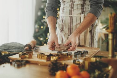 Elleri zencefilli ekmek hamurunu oklavayla yoğuruyor, baharat pişiriyor, kırsal masada süslü Noel ağacına karşı şenlikli süslemeler yapıyor. Noel kurabiyesi yapan adam, tatil zamanı.