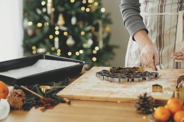 Adam Noel kurabiyesi yapıyor, atmosferik tatil zamanı. Kırsal masada zencefilli ekmek hamuru ve bayram süslemeleri ile şık Noel ağacı kesen eller.