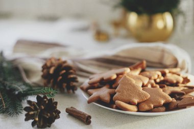 Tabakta taze zencefilli kurabiye, köknar dalları, çam kozalakları ve modern tezgahta sıcak güneş ışığı altında peçete. Lezzetli Noel kurabiyeleri yapmak, atmosferik tatil zamanı