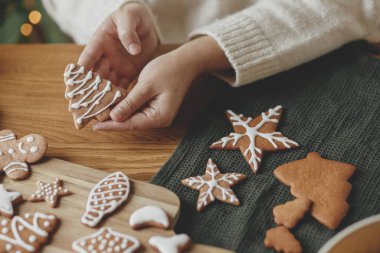 Ellerinde zencefilli kurabiye ağacı ve kırsal ahşap masa kreması var. Atmosferik Noel gelenekleri, aile zamanı. Kurabiyeleri şekerle süsleyen kadın.