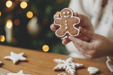 Ellerinde zencefilli kurabiye ve arka planda Noel ağacı altın ışıklarının kreması var. Atmosferik Noel tatili, aile zamanı. Kurabiyeleri şekerle süslemek