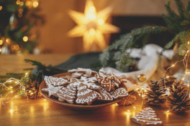 Mutlu Noeller! Ahşap masa üzerinde kremalı zencefilli kurabiye ve Noel 'in altın ışıklarına karşı şenlikli süslemeler. Atmosferik Noel arifesi, aile zamanı.