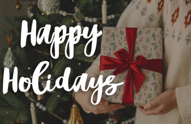 Modern dekore edilmiş vintage ağacında kırmızı kurdeleli şık bir Noel hediyesi üzerine Mutlu Tatiller metni. Mutlu noeller. Sezonun tebrik kartı. El yazısı işareti