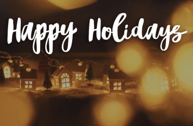 Mutlu tatiller, akşamları ışıkları bokeh olan minyatür Noel köyünde. Mutlu noeller. Sezonun tebrik kartı. El yazısı işareti