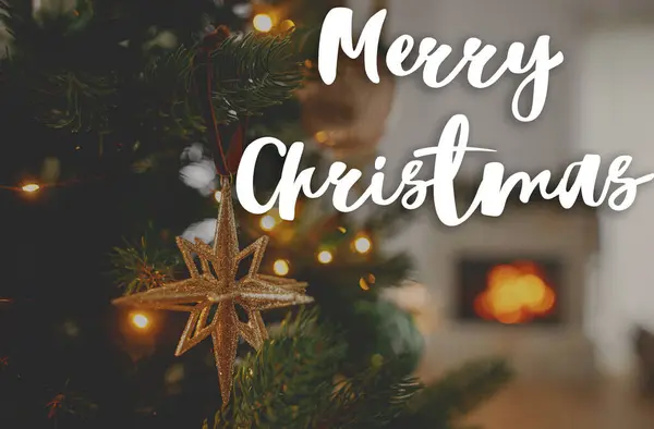 木の上のスタイリッシュなクリスマスゴールドスターのメリークリスマステキストは 暖炉を燃やすことに対して近づいています 美しい装飾されたクリスマスツリー ハッピーホリデー シーズンのグリーティングカード 手書きのサイン — ストック写真