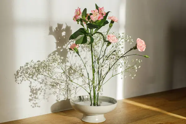Beautiful pink and white flowers in bowl on rustic background. Tender floral composition on kenzan or flower pin in sunlight. Modern flower arrangement