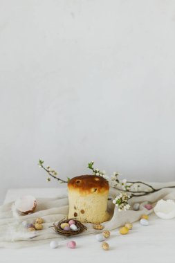 Mutlu Paskalyalar! Yuvada zarif paskalya çikolatası yumurtaları, bahar çiçekleri, geleneksel ekmek ve kırsal ahşap masada keten kumaş. Paskalya modern basit afiş, metin için yer. Mevsimler selamlar