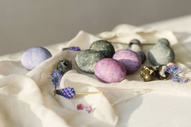 Mutlu Paskalyalar! Paskalya yumurtaları ve bahar çiçekleri sade beyaz masa üzerinde keten kumaş üzerinde. Paskalya modern basit afiş, metin için yer. Doğal boyanmış mermer ve mor yumurtalar hala hayattadır.