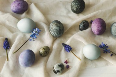 Mutlu Paskalyalar! Paskalya yumurtaları ve bahar çiçekleri sade beyaz masa üzerinde keten kumaş üzerinde. Paskalya modern basit afiş, metin için yer. Doğal boyanmış mermer ve mor yumurtalar hala hayattadır.