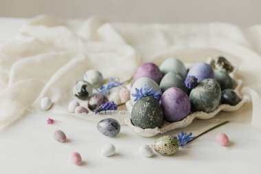Mutlu Paskalyalar! Modern tepside paskalya yumurtaları ve kırsal beyaz masada keten kumaş üzerinde bahar çiçekleri. Paskalya bayrağı, metin için yer. Doğal boyanmış mermer ve mor yumurtalar hala hayattadır.