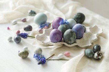 Modern tepside şık paskalya yumurtaları, yumuşak bahar çiçekleri ve kırsal beyaz masa üzerinde keten kumaş. Mutlu Paskalyalar! Doğal boyanmış mermer ve mor yumurtalar hala hayattadır. Mevsimler selamlar