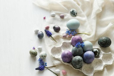 Modern tepside şık paskalya yumurtaları, yumuşak bahar çiçekleri ve kırsal beyaz masa üzerinde keten kumaş. Mutlu Paskalyalar! Doğal boyanmış mermer ve mor yumurtalar hala hayattadır. Mevsimler selamlar