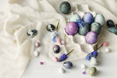 Modern tepside şık paskalya yumurtaları, yumuşak bahar çiçekleri ve kırsal beyaz masa üzerinde keten kumaş. Mutlu Paskalyalar! Doğal boyanmış mermer ve mor yumurtalar hala hayattadır. Mevsimler selamlar