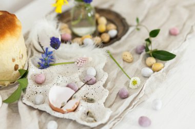 Renkli paskalya çikolatası yumurtaları, paskalya ekmeği, bahar çiçekleri ve ahşap masa üzerinde keten kumaş. Paskalya modern basit dekorasyon ve ev yapımı geleneksel pasta. Mutlu Paskalyalar!