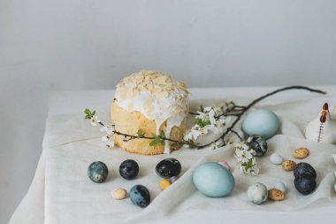 Mutlu Paskalyalar! Paskalya yumurtaları, ev yapımı paskalya ekmeği ve çarşaf peçetesinin üzerindeki bahar çiçekleri duvardaki kırsal masada. Doğal boyanmış mavi ve mermer yumurtalar ve kiraz çiçekleri durgun hayat verir.