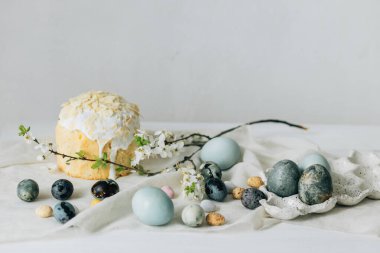 Mutlu Paskalyalar! Paskalya yumurtaları, ev yapımı paskalya ekmeği ve çarşaf peçetesinin üzerindeki bahar çiçekleri duvardaki kırsal masada. Doğal boyanmış mavi ve mermer yumurtalar ve kiraz çiçekleri durgun hayat verir.