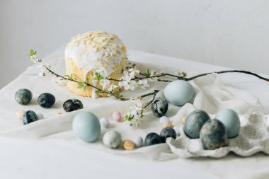 Mutlu Paskalyalar! Paskalya yumurtaları, ev yapımı paskalya ekmeği ve çarşaf peçetesinin üzerindeki bahar çiçekleri duvardaki kırsal masada. Doğal boyanmış mavi ve mermer yumurtalar ve kiraz çiçekleri durgun hayat verir.