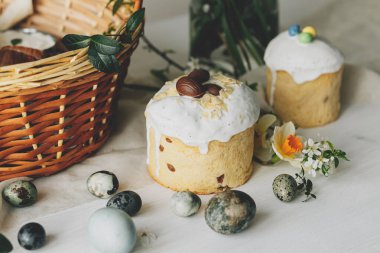Paskalya ekmekleri, yumurtalar ve sepette kırsal masada bahar çiçekleri. Mutlu Paskalyalar! Geleneksel Paskalya bayramı yemekleri. Modern doğal boya yumurtaları, nergisler ve kiraz çiçekleri.