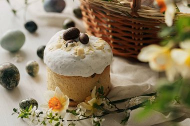 Paskalya ekmekleri, yumurtalar ve sepette kırsal masada bahar çiçekleri. Mutlu Paskalyalar! Geleneksel Paskalya bayramı yemekleri. Modern doğal boya yumurtaları, nergisler ve kiraz çiçekleri.