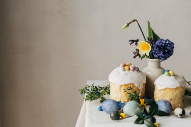 Paskalya yumurtaları, panettone, bahar çiçekleri ve kırsal ahşap masada çikolatalı yumurtalar. Doğal boya mermer yumurta, çiçek ve bayram yemeği. Mesaj için yer var. Mutlu Paskalyalar!