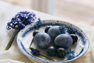 Mutlu Paskalyalar! Klasik tabakta paskalya yumurtaları keten peçetede bahar çiçekleri, kırsal masa ortamları. Doğal boyalı mavi yumurtalar ve sümbül çiçekleri. Modern durgun yaşam