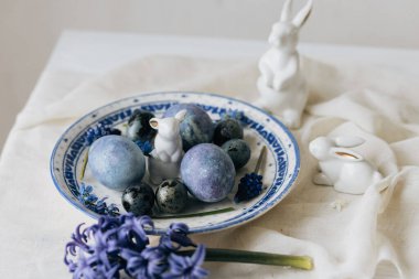 Mutlu Paskalyalar! Klasik tabakta paskalya yumurtaları, tavşan ve keten peçetede bahar çiçekleri, kırsal masa ayarı. Doğal boyalı mavi yumurtalar ve sümbül çiçekleri. Modern durgun yaşam