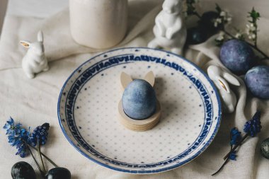 Paskalya sofrası çok şık. Tavşan heykelciğinde paskalya yumurtası, klasik tabakta ve kırsal masada bahar çiçekleri. Mutlu Paskalyalar! Doğal boya mavi yumurta ve mor hiacynt. Tatil için en az yaşam süresi