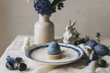 Paskalya sofrası çok şık. Tavşan heykelciğinde paskalya yumurtası, klasik tabakta ve kırsal masada bahar çiçekleri. Mutlu Paskalyalar! Doğal boya mavi yumurta ve mor hiacynt. Tatil için en az yaşam süresi