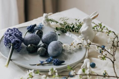 Mutlu Paskalyalar! Klasik tabakta paskalya yumurtaları, tavşan ve keten peçetede bahar çiçekleri, kırsal masa ayarı. Doğal boyalı mavi yumurtalar ve sümbül çiçekleri. Modern durgun yaşam