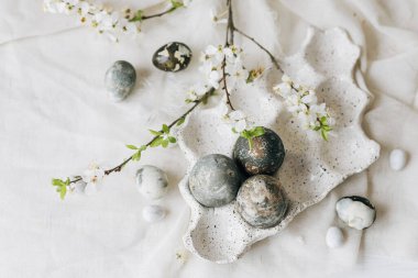 Mutlu Paskalyalar, düzlük. Paskalya yumurtaları ve bahar çiçekleri keten kırsal masada. Tepside doğal boyanmış mermer yumurtalar ve kiraz çiçekleri. Modern minimal düz yatak