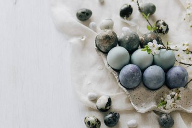Mutlu Paskalyalar! Paskalya yumurtaları ve bahar çiçekleri keten kırsal masada. Doğal boyalı mermer mavi yumurtalar tepside ve kiraz çiçekleri. Modern minimal düz yatak