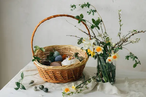 Yumurtalı Paskalya sepeti ve kırsal masada bahar çiçekleri. Mutlu Paskalyalar! Geleneksel Paskalya bayramı yemekleri. Modern doğal boya yumurtaları, lezzetli jambon, ekmek, tereyağı, pancar.