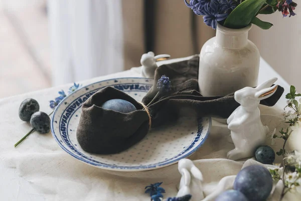 Mutlu Paskalyalar! Tavşan peçetesindeki paskalya yumurtası vintage tabak ve keten peçetedeki bahar çiçekleri, kırsal masa ayarı. Doğal boyalı mavi yumurtalar ve sümbül çiçekleri. Modern durgun yaşam