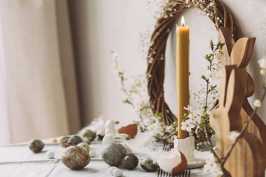 Mutlu Paskalyalar! Şık paskalya yumurtaları, ahşap tavşanlar, kiraz çiçekleri ve kır masasında mum. Modern doğal boyanmış mermer yumurta ve bahar çiçekleri. Paskalya 'da kırsal evdeki hayat dekorasyonu